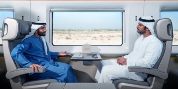 Two passengers seated across a table inside an Etihad Rail passenger train