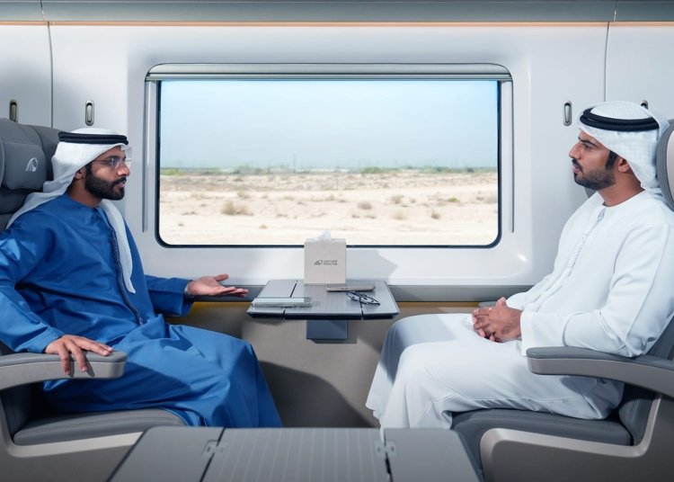 Two passengers seated across a table inside an Etihad Rail passenger train