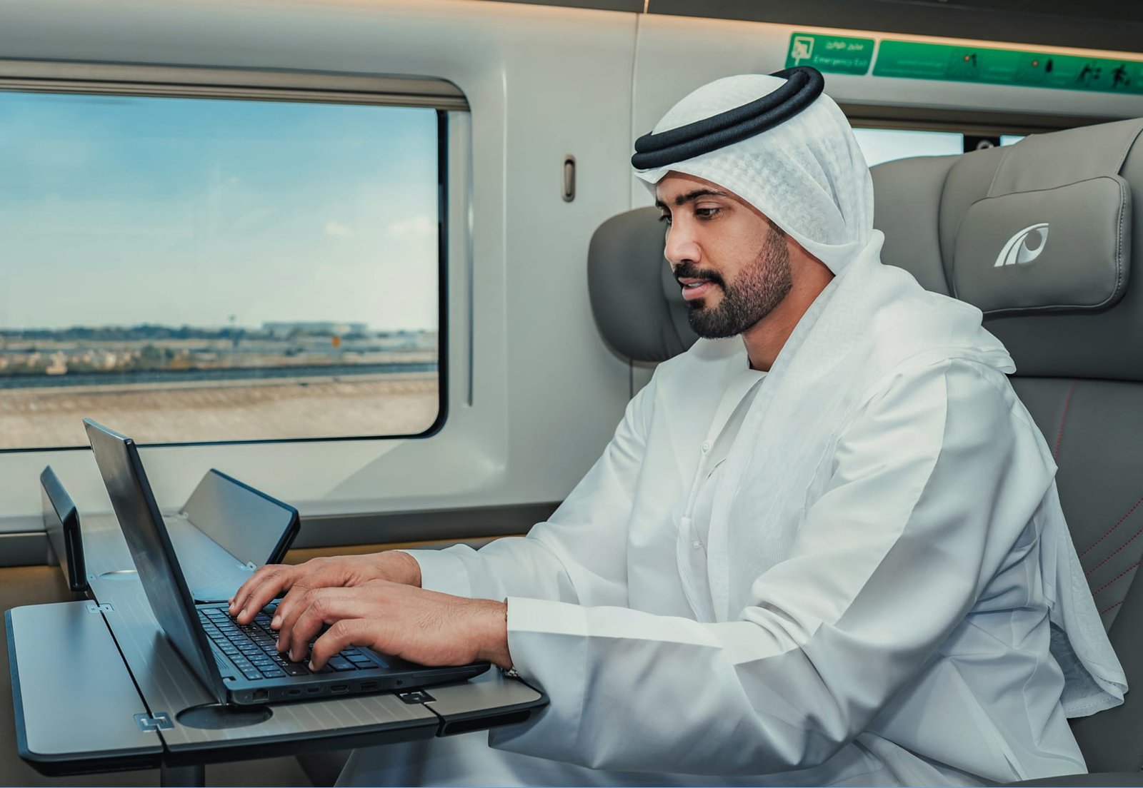 Passenger using a laptop at a table inside an Etihad Rail train