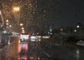 Raindrops on a windscreen with cars and streetlights on a wet road at night